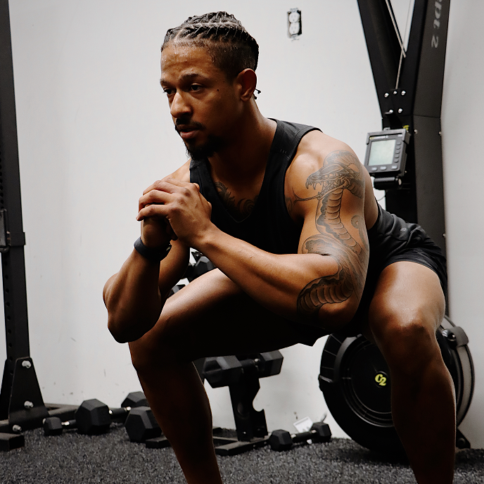Man in a gym squatting with weights and exercise equipment in the background