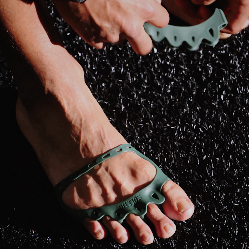 Person wearing green toe separators on a dark surface