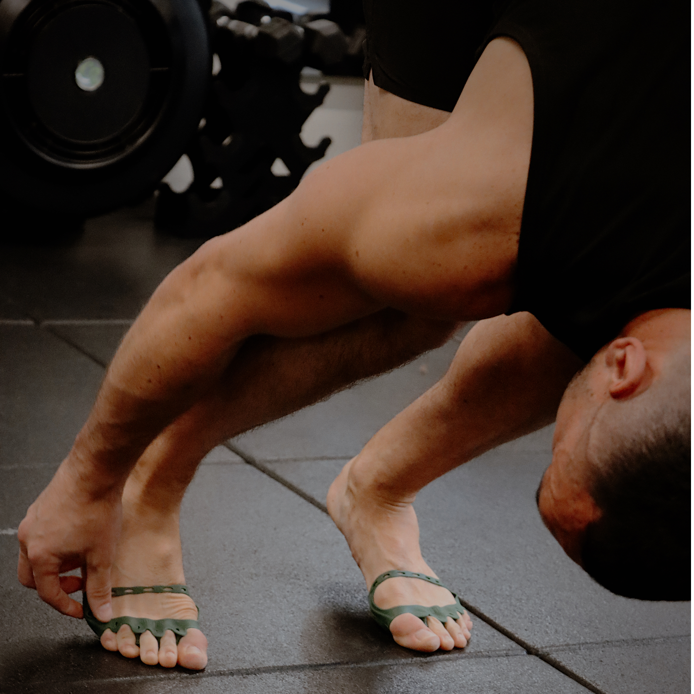 Person wearing green toe spacers on a gym floor with weights in the background